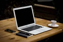 En dator som står på ett bord med en kaffe intill.