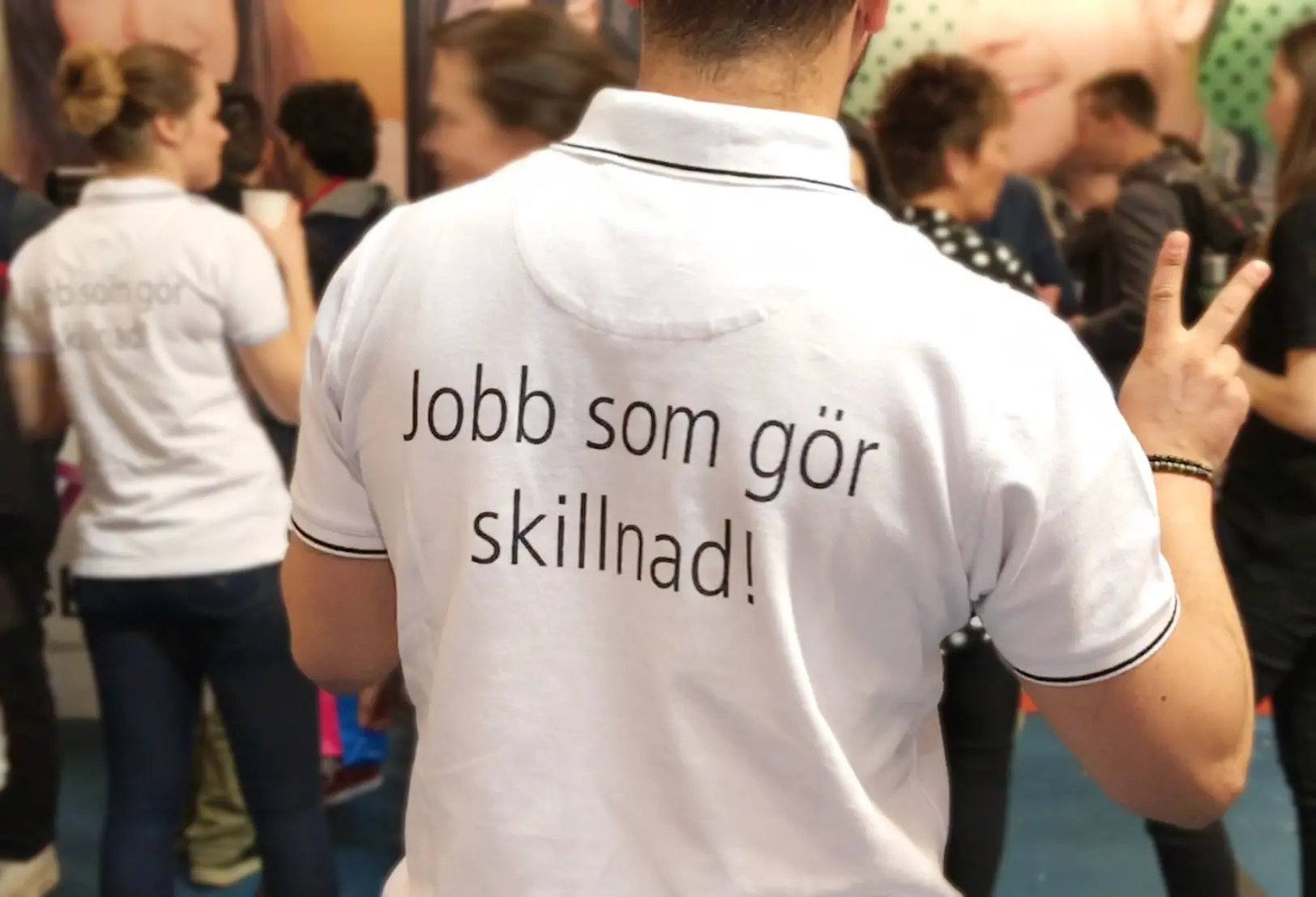Ryggen på en anställd på rekryteringsmässan där texten "Jobb som gör skillnad" står i svart text på den vita t-shirten.